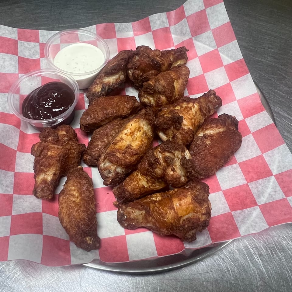 Crispy fried chicken wings with barbecue and ranch dipping sauces on red and white checkered paper.