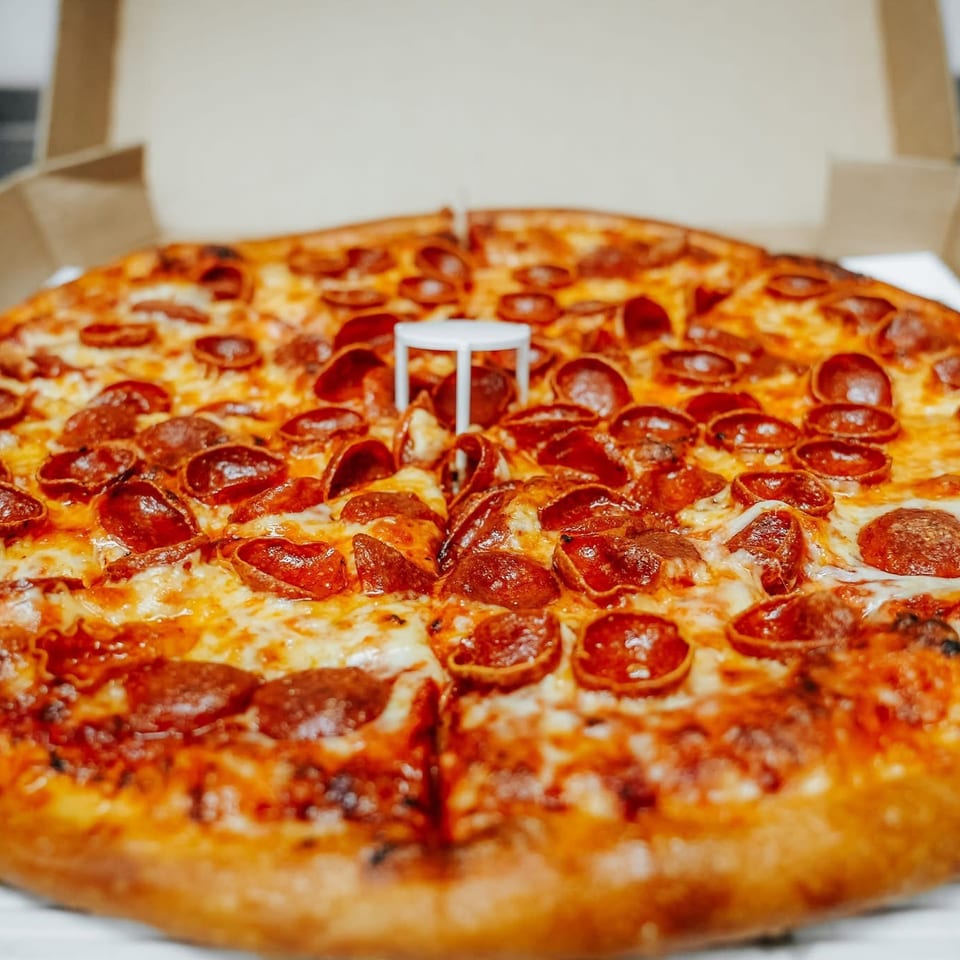 A whole pepperoni pizza with melted cheese in an open cardboard delivery box.