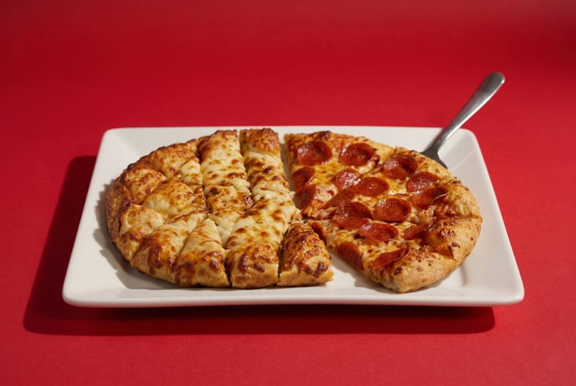 A white rectangular plate holds half a pepperoni pizza and half an order of cheesy breadsticks.