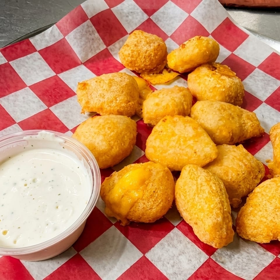 Golden-fried cheese curds and a side of ranch dressing on red and white checkered paper.
